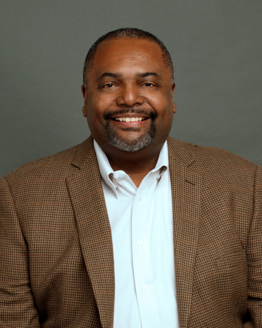 A man in a brown jacket and white shirt.