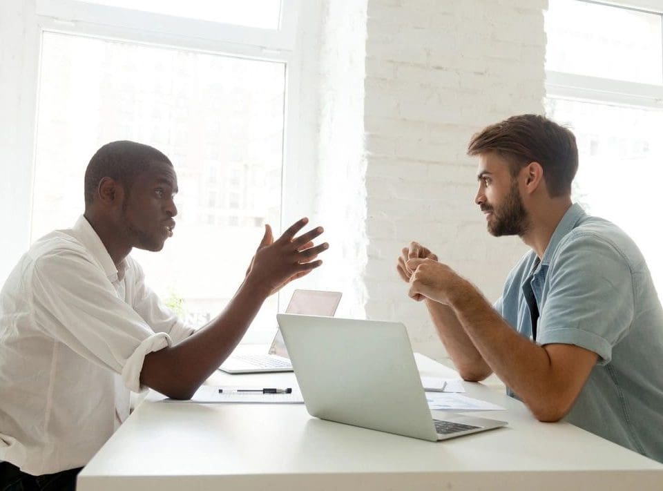 Two men sitting at a table with laptops