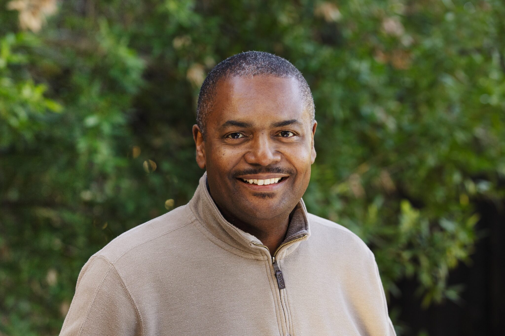 A man in a tan jacket smiling for the camera.