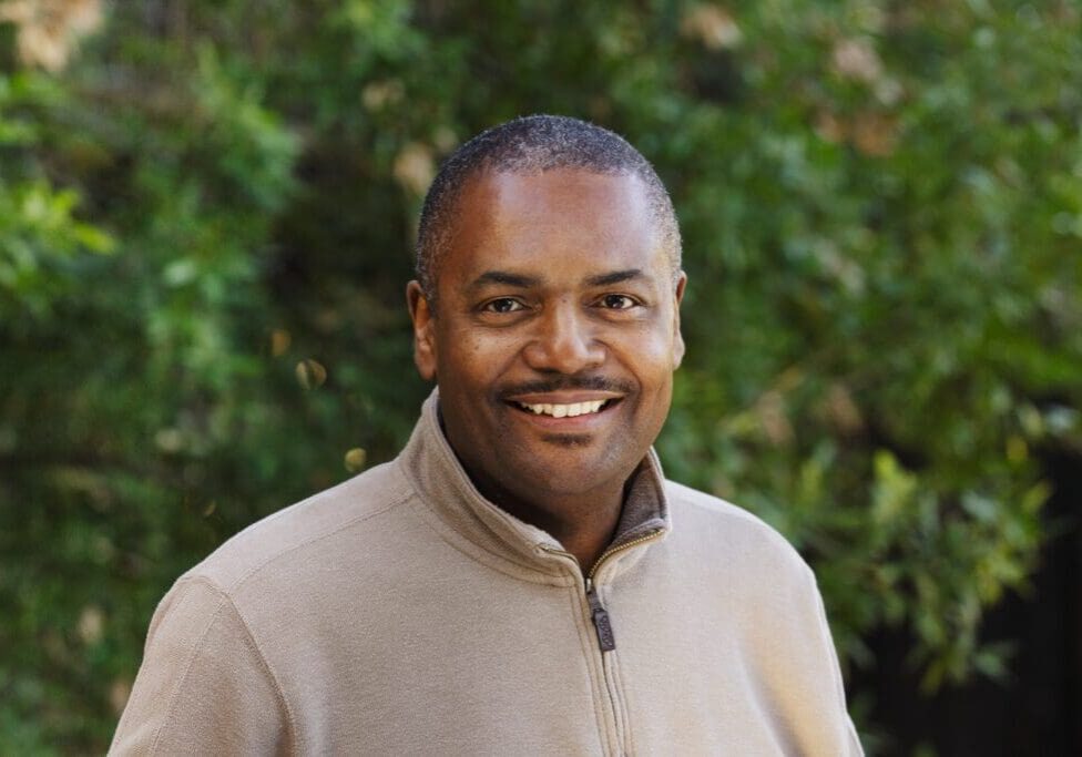 A man in a tan jacket smiling for the camera.